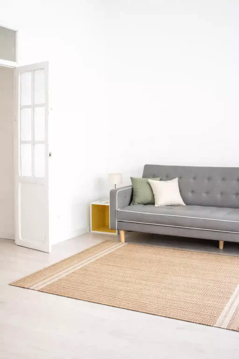 A small sunlit living room featuring a natural jute rug and sage green pillows, showcasing summer 2026 rugs for small spaces.