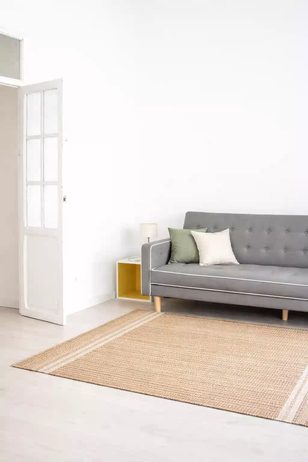 A small sunlit living room featuring a natural jute rug and sage green pillows, showcasing summer 2026 rugs for small spaces.