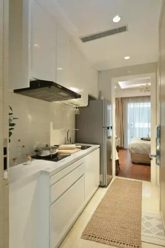 A modern white kitchen featuring summer 2026 rugs for small spaces, specifically a natural jute runner and a washable entryway mat for high-traffic durability.