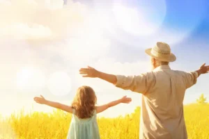 Human-Centric Lighting scene: a young girl and an elderly man in a sunlit field, arms outstretched — symbolizing freedom, nature, vitality, and intergenerational harmony.