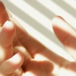 Human hand in compact space illuminated by sunlight through blinds, highlighting skincare and UV exposure risks.