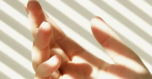 Human hand in compact space illuminated by sunlight through blinds, highlighting skincare and UV exposure risks.
