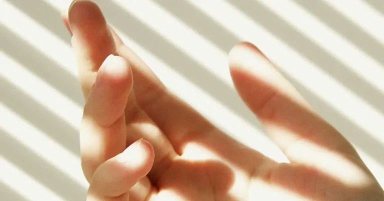 Human hand in compact space illuminated by sunlight through blinds, highlighting skincare and UV exposure risks.